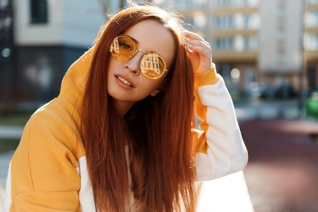 Portret van een charmante vrouw met rood haar met een zonnebril op de zomerstraat