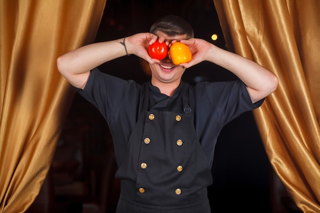 Portret van een chef-kok die zijn ogen dichtdeed met een tomaat en een handjevol peper