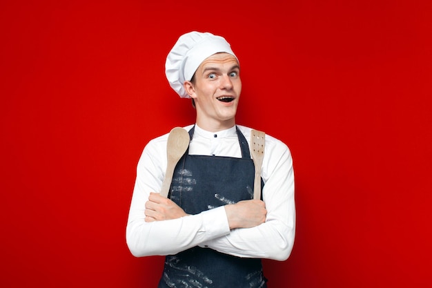 Portret van een chef-kok op een rode geïsoleerde achtergrond keukenmedewerker in uniform met keukengerei