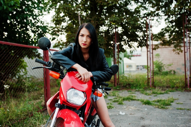 Portret van een coole en geweldige vrouw in jurk en zwart lederen jas zittend op een koele rode motor.