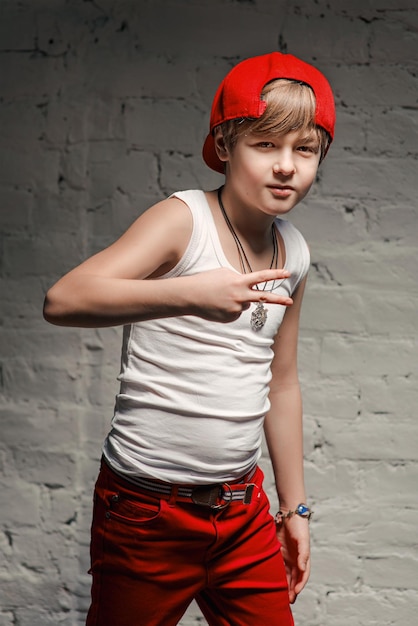 Portret van een coole jonge hiphopjongen in een rode hoed en een rode broek en een wit overhemd in de loft