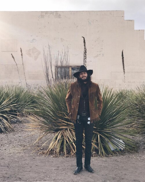 Foto portret van een cowboy die bij een plant tegen de muur staat