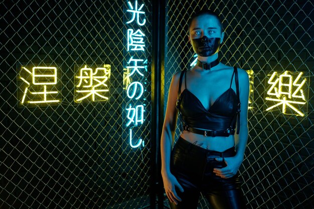 Portret van een cyberpunk-vrouw die in een leren tanktop en een broek staat die naar de camera kijkt met hiërogliefen die nirvana en het westerse paradijs op de achtergrond betekenen