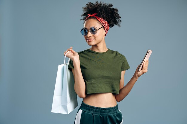 Portret van een dolblije enthousiaste vrouw die een boodschappentas vasthoudt, zich geweldig voelt met een pakket en een smartphone bij haar hand houdt terwijl ze wegkijkt. Black Friday-concept