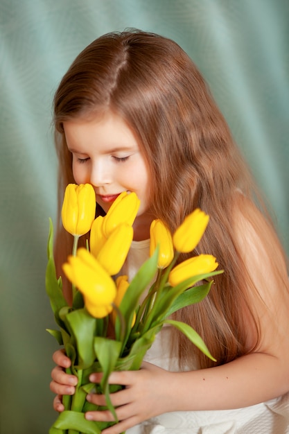 Portret van een donkerbruin kindmeisje met boeket van gele tulpen op een blauwe achtergrond