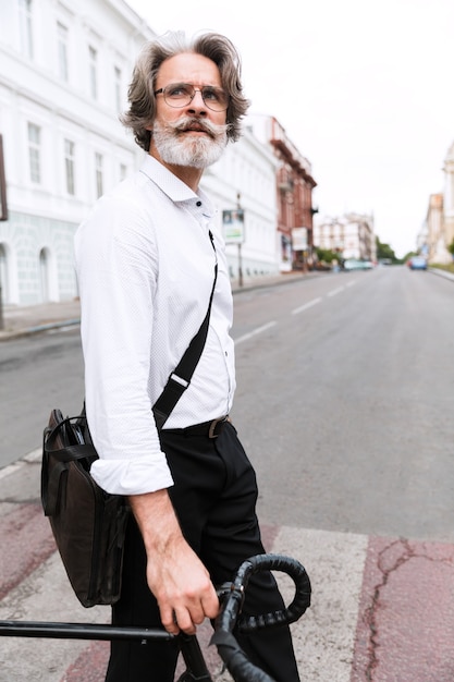 Foto portret van een doordachte volwassen zakenman in een bril die met de fiets op straat in de stad loopt