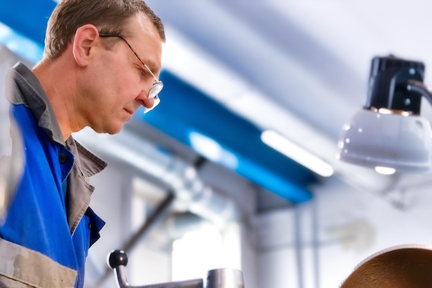 Portret van een draaier met een bril van 5055 jaar oud op het werk Oudere metalen draaier werkt in de werkplaats aan een machine achter het werk