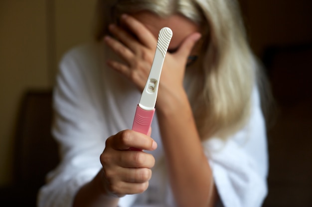 Portret van een droevige jonge vrouw die zwangerschapstest bekijkt met slecht nieuws