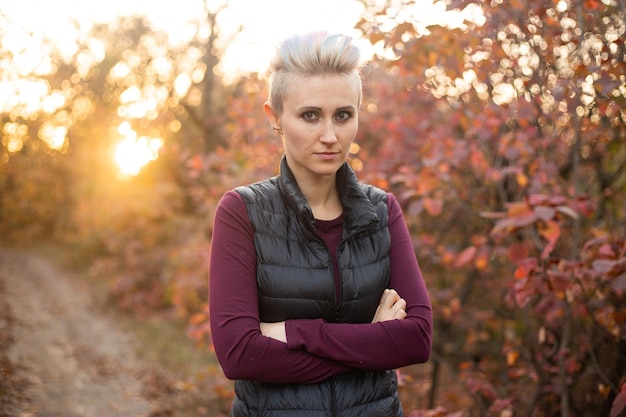 Portret van een droevige vrouw met kort haar op een herfstbosachtergrond met gouden en rode bomen