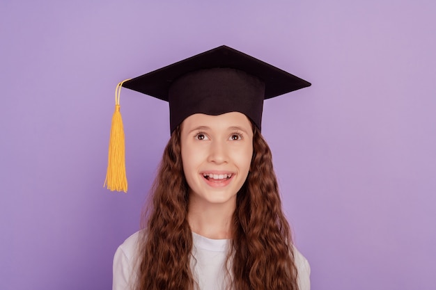 Portret van een dromerig, grappig meisje dat een lege lege ruimte opzoekt opgewonden gezicht draagt een vrijgezellenhoed op een paarse achtergrond