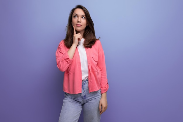 Portret van een dromerige jonge vrouw met donkerbruin haar in spijkerbroek tegen een paarse muur