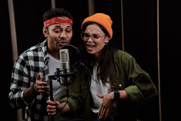 Portret van een duet van een jonge man en een vrouw die zingen in een condensatormicrofoon terwijl ze een nummer opnemen in