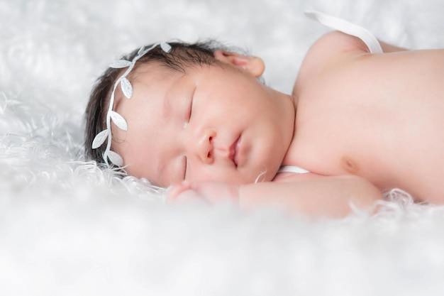 Portret van een één maand oud slapend, pasgeboren babymeisje. ze draagt een hoofdband met een kroon en slaapt op een witte deken. concept portret studio mode pasgeboren.