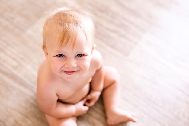 Portret van een eenjarige kind zittend op de vloer. Mooie kleine jongen thuis