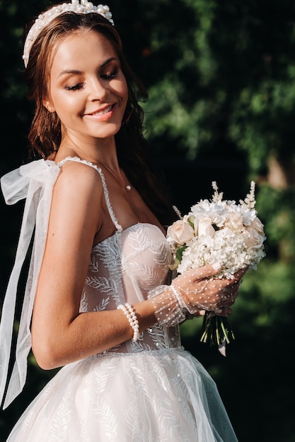 Portret van een elegante bruid in een witte jurk met een boeket in de natuur in een natuurpark. model in een trouwjurk en handschoenen en met een boeket. wit-rusland