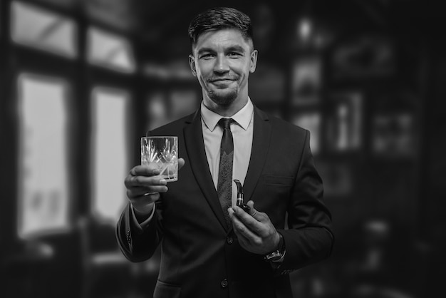 Portret van een elegante man in een pak met een rookpijp en een glas in een restaurant. Bedrijfsconcept. Gemengde media