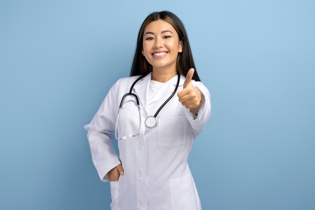Portret van een enthousiaste aziatische arts die duimen opsteekt en opgewonden glimlacht