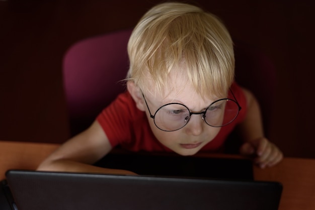 Portret van een ernstige blonde jongen met een bril met behulp van een laptop