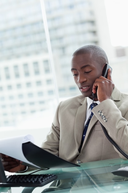 Portret van een ernstige ondernemer die een telefoongesprek maakt terwijl het lezen van een document