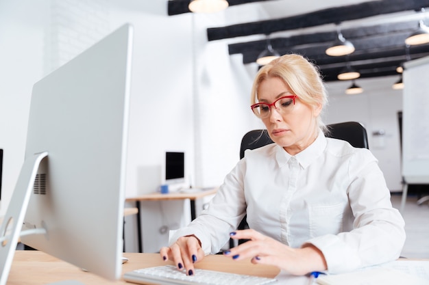 Portret van een ernstige rijpe onderneemster die op bureau met computer werkt