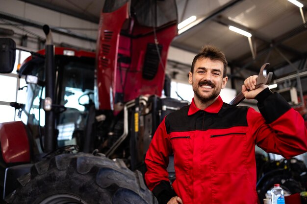 Portret van een ervaren militair die in een werkplaats staat In de achtergrond een tractor met geopende kap