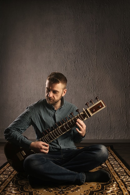 Foto portret van een europese man die de sitar op het tapijt speelt