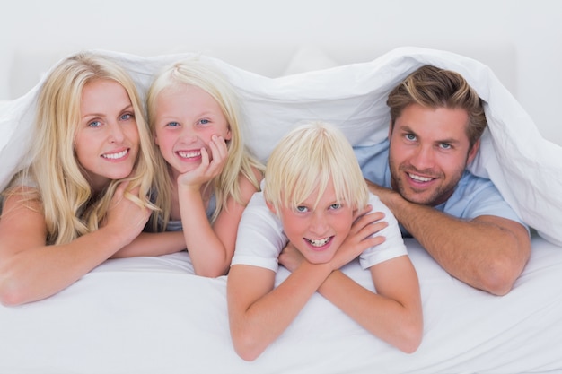 Portret van een familie die onder dekbed glimlacht