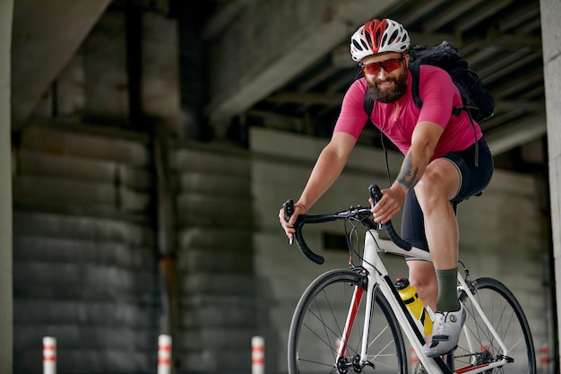 Portret van een fietser die onder een brug staat met een fiets in zijn hand die voor de camera poseert tegen een architectuurachtergrond Actieve levensstijl Fietsen is een hobby