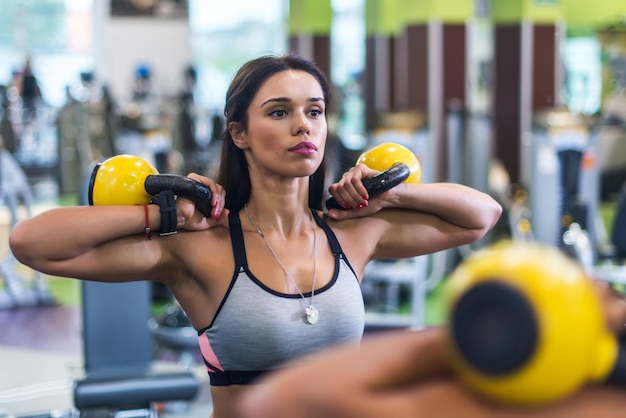 Portret van een fitte vrouw die naar een spiegel kijkt die traint met de kettlebell in de sportschool