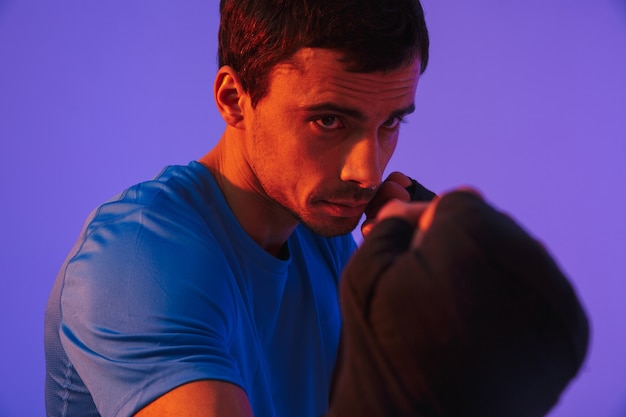 Portret van een fitte zelfverzekerde sportman die boksoefeningen doet die over een violette muur worden geïsoleerd