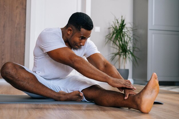 Portret van een flexibele afro-amerikaanse man die yoga beoefent terwijl hij in janu sirsasana-oefening zit