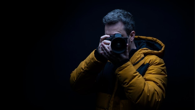 Portret van een fotograaf in een gele winterjas die een foto maakt met een zwarte achtergrond in de studio