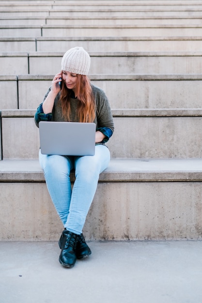 Portret van een freelancer-vrouw die laptop en smartphone gebruikt terwijl ze op de trap in de stadsstraat zit