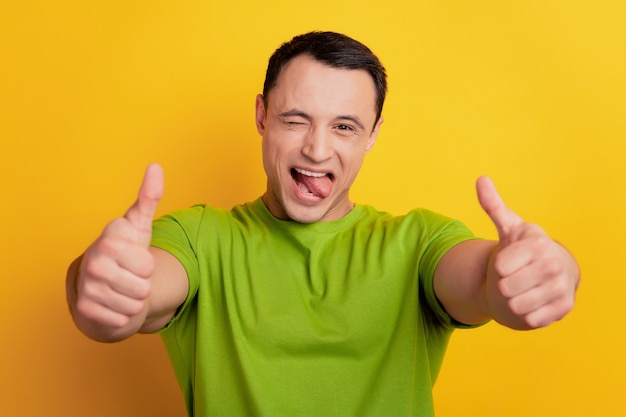 Portret van een funky man steekt twee duimen omhoog open mond steekt tong uit op gele achtergrond