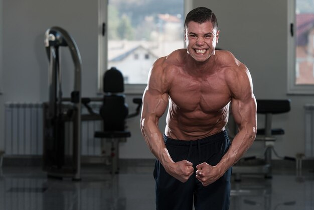 Portret van een fysiek fitte man die zijn goed getrainde lichaam in de sportschool laat zien