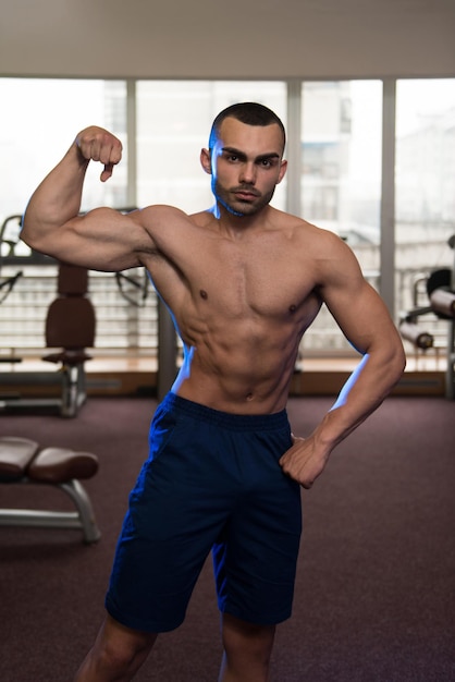 Portret van een fysiek fitte man die zijn goed getrainde lichaam in de sportschool laat zien