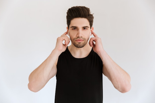 Portret van een geconcentreerde jonge sportman geïsoleerd over een witte muur die muziek luistert met een koptelefoon.