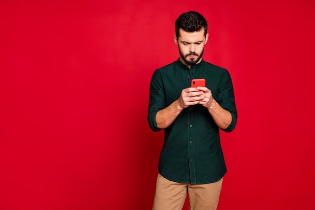 Portret van een geconcentreerde man gebruikt zijn smartphone om werkproblemen op sociaal netwerk op te lossen, draag een bruine broek in casual stijl