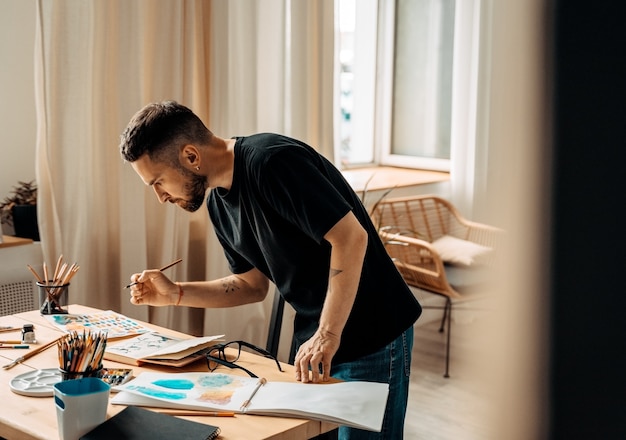 Portret van een geconcentreerde mannelijke kunstenaar die bij een tafel staat te tekenen in een schilderles in een studio