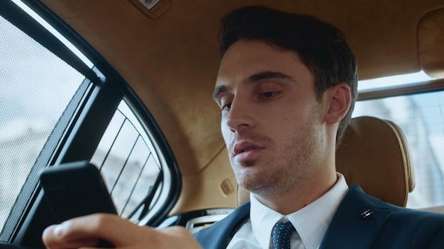 Portret van een gefocuste zakenman die een bericht op de telefoon schrijft in een luxe auto