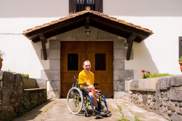 Portret van een gehandicapte in het geel gekleed in een rolstoel glimlachend bij de ingang van zijn huis