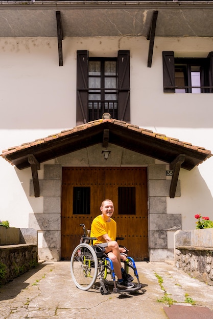 Portret van een gehandicapte in het geel gekleed in een rolstoel glimlachend bij de ingang van zijn huis