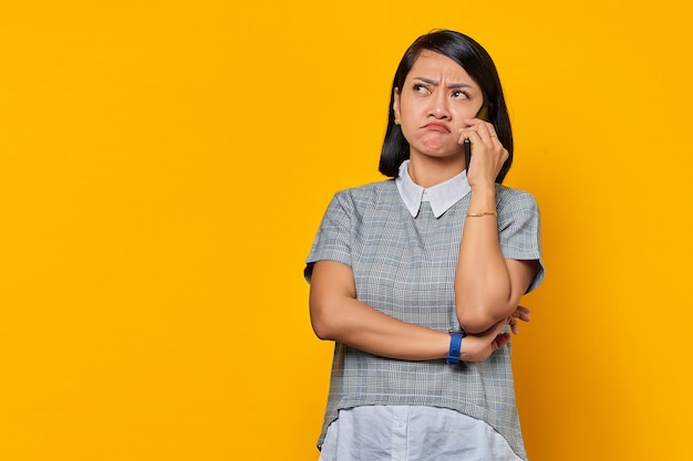 Portret van een geïrriteerde jonge Aziatische vrouw die een inkomende oproep op een smartphone ontvangt en opzij kijkt op een gele achtergrond