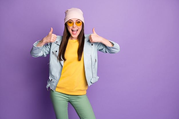 Portret van een gek energiek jeugdmeisje dat geniet van optie-promotie-advertenties toont duim-omhoog aanbevolen keuzebeslissingen draag een geelgroene broek geïsoleerd over een violette kleurachtergrond