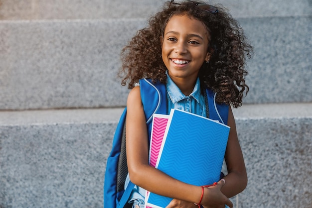 Portret van een gelukkig Afrikaans schoolmeisje met rugzak met notitieboekjes buiten de basisschool