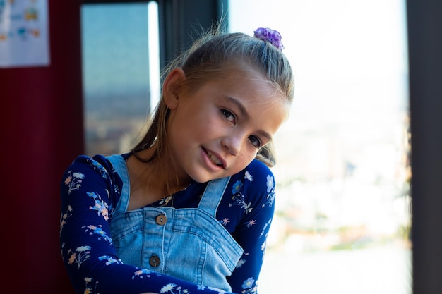 Foto portret van een gelukkig blank schoolmeisje dat bij het raam zit in een klaslokaal op de basisschool