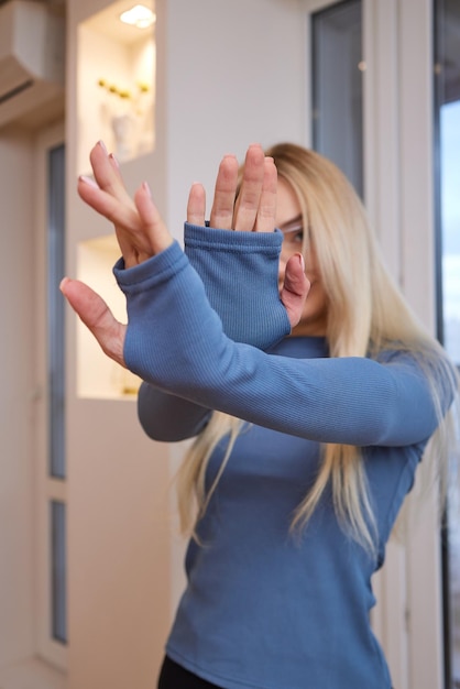 Portret van een gelukkig charmant, vrolijk blond meisje met een bril glimlacht die er gelukkig en blij uitziet levendig met natuurlijke make-up gebruind gekleed in een casual lichtblauw t-shirt met lange mouwen