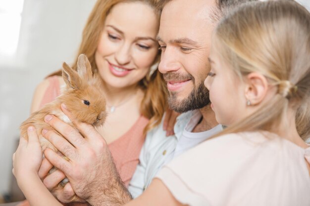 Foto portret van een gelukkig gezin met één kind dat speelt met een schattig pluizig konijn