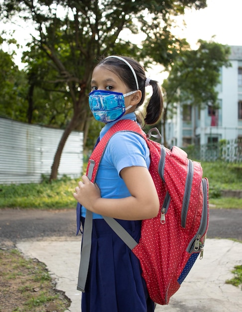 Foto portret van een gelukkig indiase meisje kind student in schooluniform neusmasker bescherming naar school gaan