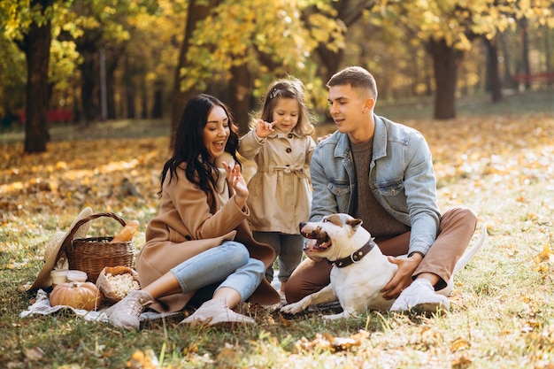 Portret van een gelukkig jong gezin dat samen op de deken zit en met de hond speelt in het herfstpark